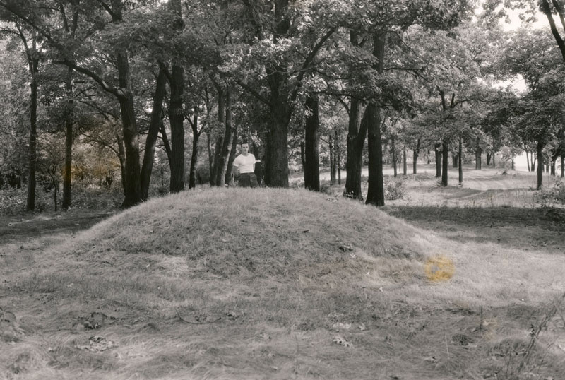 A man poses behind a conical Native American burial mound near the west end of Picnic Point on the University of Wisconsin-Madison campus.
